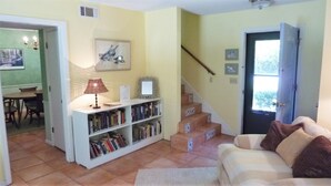 A living room with a sofa, a bookshelf, a lamp, and a staircase. - Ariel East Duplex 3 bedrooms, 2.5 bathrooms (Jekyll Island)