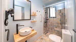 Une salle de bain moderne dotée d’un grand miroir, d’un lavabo sur colonne, d’une douchette à main et d’une douche à l’italienne avec des carreaux à motifs.