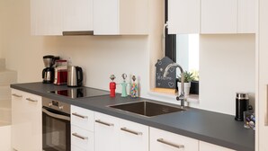 Une cuisine moderne avec des meubles blancs, un plan de travail noir, des appareils en acier inoxydable et une petite fenêtre ornée d’une pancarte accueillante.