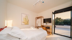 Une chambre moderne avec un grand lit, une commode en bois, un téléviseur à écran plat et une porte-fenêtre coulissante donnant sur un balcon avec vue sur la ville.