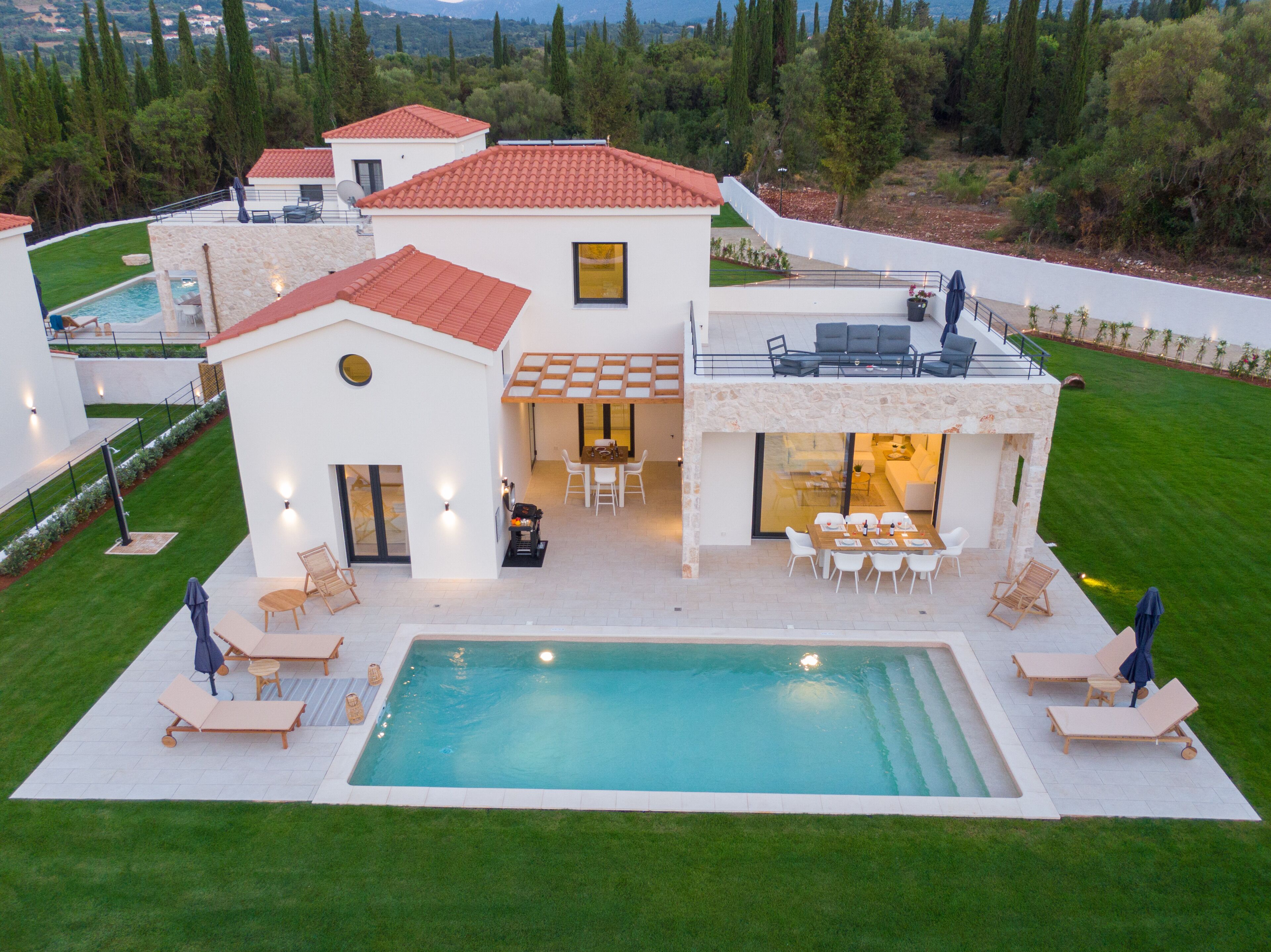 A modern villa with a swimming pool, outdoor seating, and a view of the surrounding landscape.