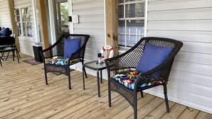 Eine überdachte Veranda mit zwei Korbstühlen und einem kleinen Tisch, mit einem Willkommensschild und einer Laterne.