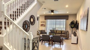 Un vaste salon doté d’un escalier, d’un ventilateur de plafond et d’une grande fenêtre avec des stores.