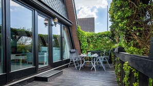 Una terrazza in legno con mobili da esterno, un ingresso con porta vetrata e vista sulla città.