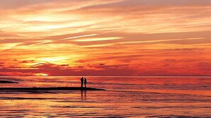Un tramonto su una spiaggia con due figure silhouettate che si ergono sulla riva.