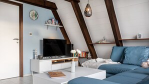 Un soggiorno moderno con televisore, mobili bianchi, libreria e divano blu.