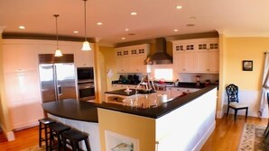 Een moderne keuken met een centraal eiland, roestvrijstalen apparatuur, hanglampen en een vloerkleed met een patroon.