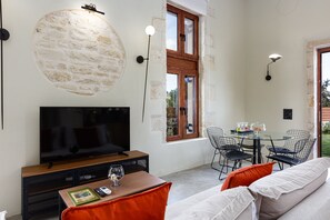 A modern living room with a flat-screen TV, a coffee table, and a sofa. There is a dining area with a glass table and chairs.