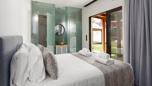 Ein Hotelzimmer mit Bett, einem Badezimmer mit Glasdusche und Blick ins Freie.