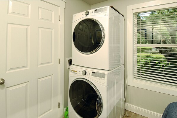 A laundry room with two stacked front-loading washing machines and a window with blinds. - Fantastic Rates! Book Now and Save* Beautiful bay front cottage! (Lillian)