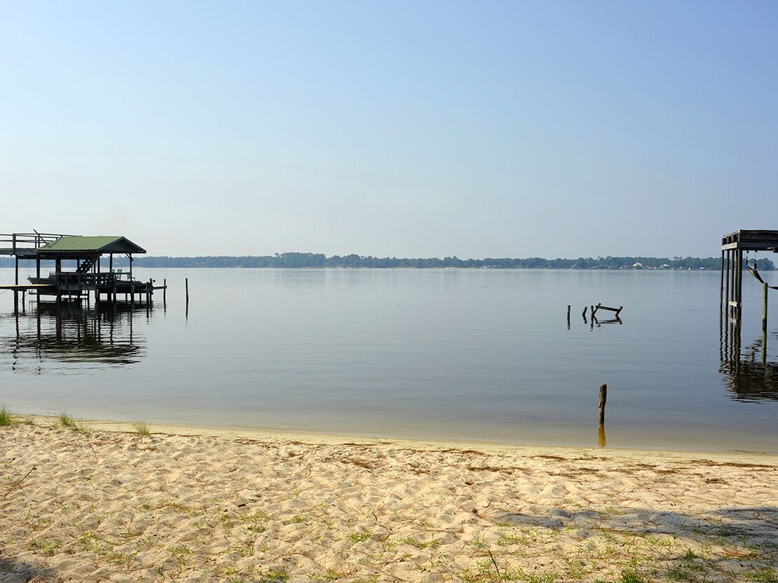Una platja amb sorra, un pontí petit i aigua tranquil·la.