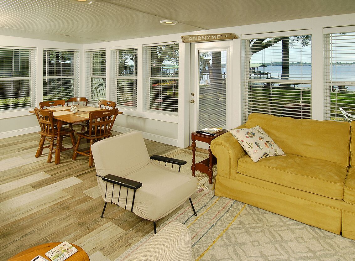 A sunroom with a dining table, chairs, a sofa, and large windows with blinds.
