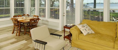 A sunroom with a dining table, chairs, a sofa, and large windows with blinds.