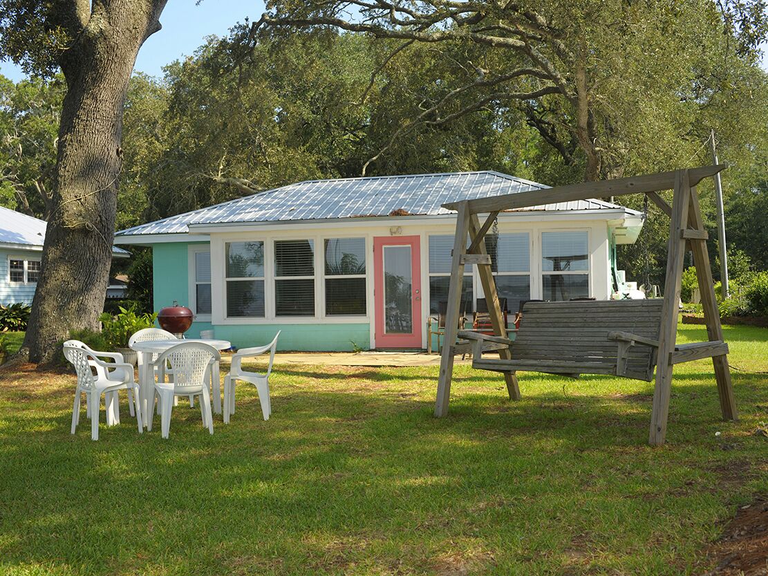Una casa con fachada verde, puerta roja y un porche con un columpio de madera.