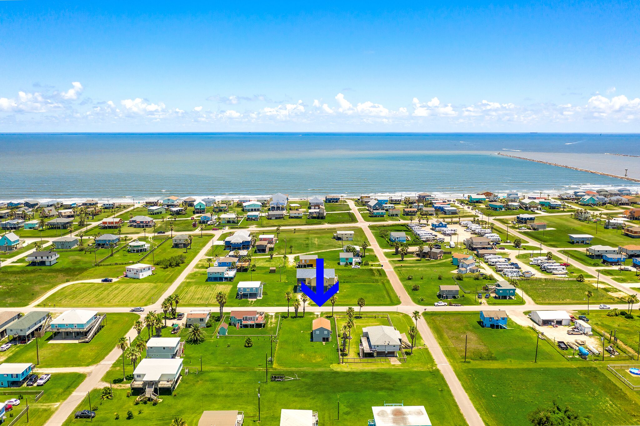 A coastal residential area with houses arranged in a grid pattern, a clear view of the ocean, and a prominent blue arrow pointing downwards.