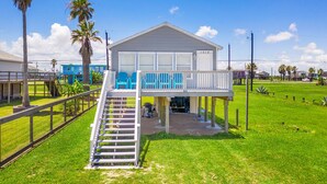 Een huis aan het strand met een overdekte veranda, een trap naar de bovenverdieping en uitzicht op de oceaan.