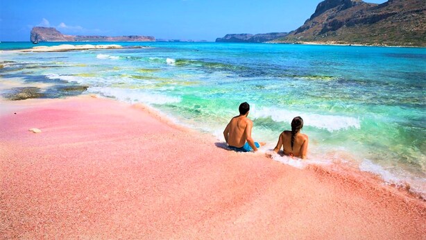 A beach with clear turquoise water and a pink sand shore.