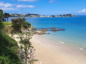 A coastal beach with clear waters, a sandy shore, and a distant town.