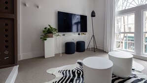 Un salon moderne avec un téléviseur à écran plat, une plante en pot, deux poufs et un tapis à motifs zébrés.
