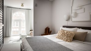 Une chambre d’hôtel moderne avec un grand lit, une chaise en bois, une petite table et une grande fenêtre avec des rideaux.