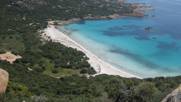 Ett kustlandskap med en sandstrand och klart, blått vatten.