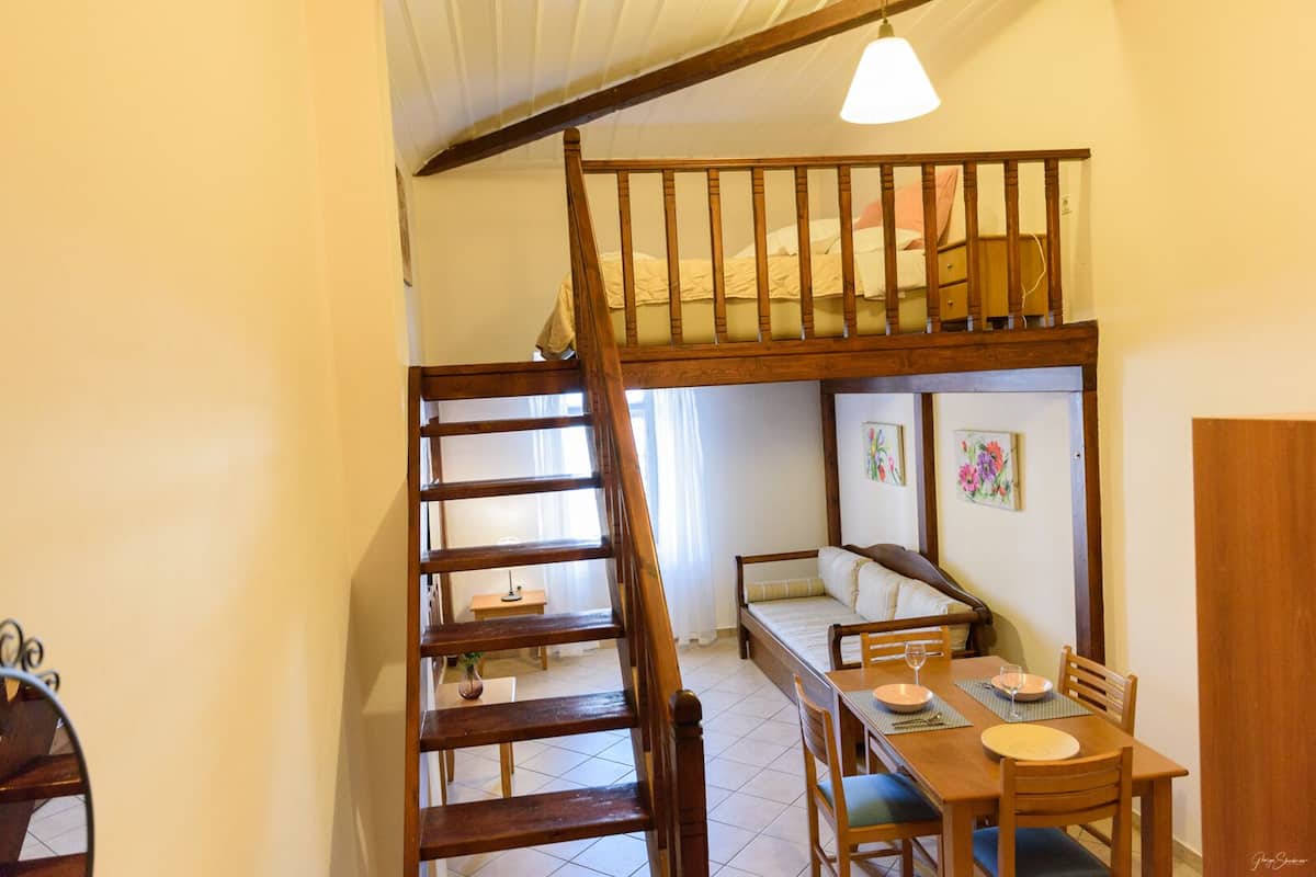 Ein Schlafzimmer im Loft-Stil mit einer Holztreppe, einem Etagenbett, einer Essecke mit Tisch und Stühlen sowie einem kleinen Fenster.