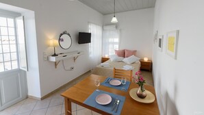 Una habitación de hotel con cama, mesitas de noche, televisor, escritorio con silla y una mesa de comedor preparada para dos.