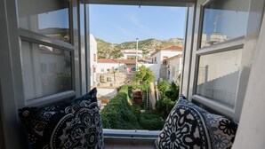 Vista desde una ventana con cojines estampados, que da a un patio con edificios y colinas.