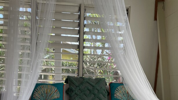 A neatly made bed with rolled white towels, teal pillows with a fan design, and white curtains. - Bak A  Yaad Cottage Lupine Cottage (Negril)