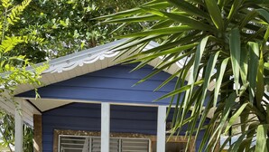A small blue house with a porch, a window with shutters, and a concrete path leading to the entrance. - Bak A  Yaad Cottage Lupine Cottage (Negril)