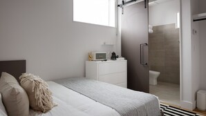 Un dormitorio moderno con cama, cómoda, tocador y zona de ducha.