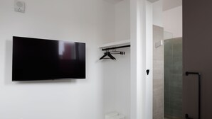 Un baño moderno con una televisión de pantalla plana en la pared, un perchero y una cabina de ducha de vidrio.