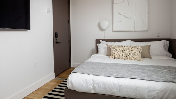 Un dormitorio con cama, una puerta, una lámpara fijada a la pared y una obra de arte abstracta enmarco.