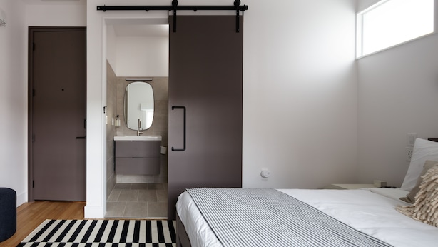 A bedroom with a bed, a nightstand, a dresser, and a sliding door leading to a bathroom. - Boutique Hotel Suite above the Jefferson Theater on the Downtown Mall (Charlottesville)