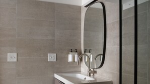A modern bathroom with a white sink, two faucets, a large mirror, and a towel rack with bottles. - Boutique Hotel Suite above the Jefferson Theater on the Downtown Mall (Charlottesville)