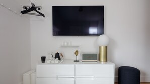 A modern living room with a flat-screen TV, white cabinetry, and a round ottoman. - Boutique Hotel Suite above the Jefferson Theater on the Downtown Mall (Charlottesville)