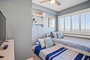 A bedroom with two beds, a TV, and a window with blinds.