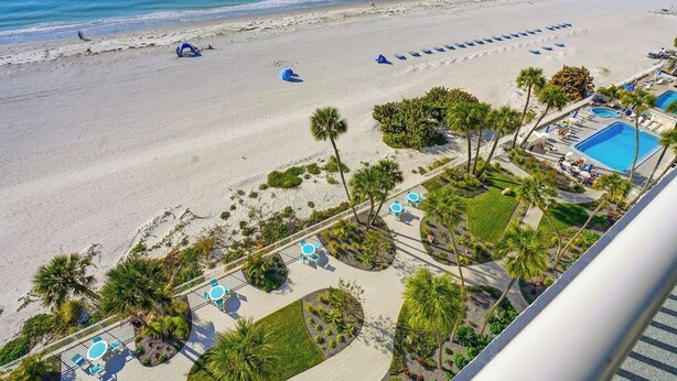 An aerial view of a beach resort with a pool area, palm trees, and a clear view of the ocean. - Beachfront  Paradise (Indian Shores)