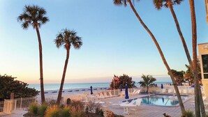 A poolside area with lounge chairs, palm trees, and a view of the ocean. - Beachfront  Paradise (Indian Shores)