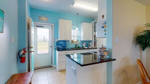 Une cuisine avec des meubles blancs, un mur d’accent bleu, un petit îlot central doté d’un évier et une porte donnant sur l’extérieur.