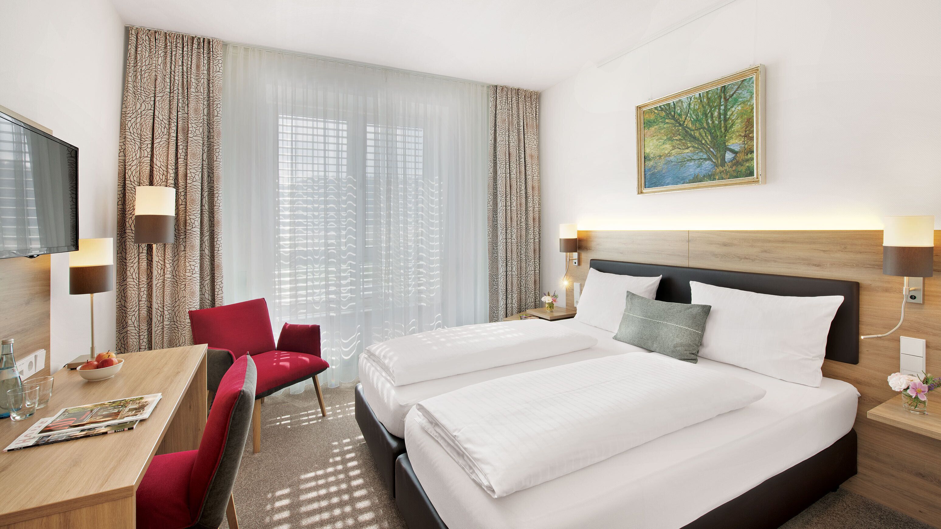 A hotel room with a large bed, a desk with a chair, a TV, and a painting on the wall.