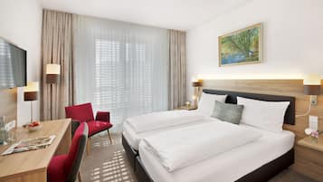 A hotel room with a large bed, a desk with a chair, a TV, and a painting on the wall.