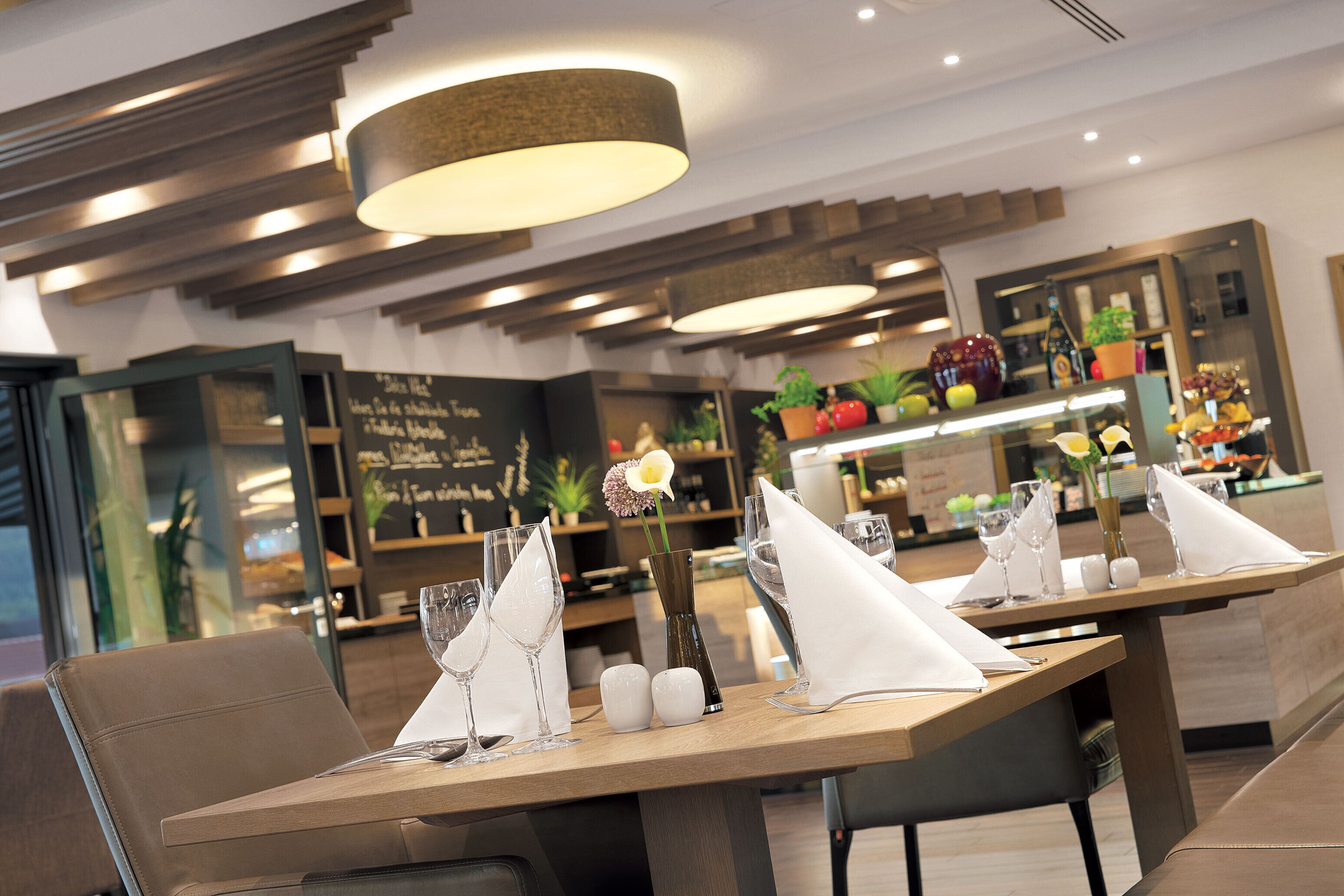 Un restaurante con decoración moderna, que cuenta con mesas y sillas de madera, y un elemento de iluminación central.