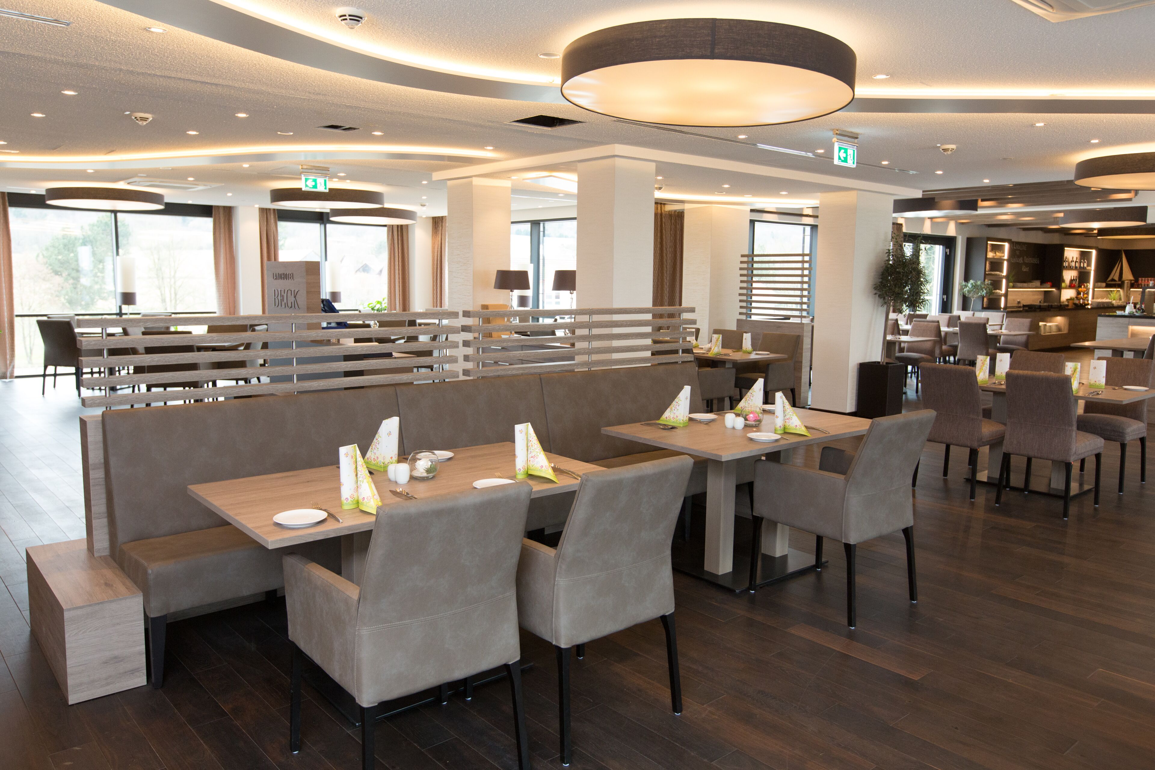 Een modern restaurant met ruimtes met zitbanken en tafels, een bar en uitzicht op het omliggende landschap.