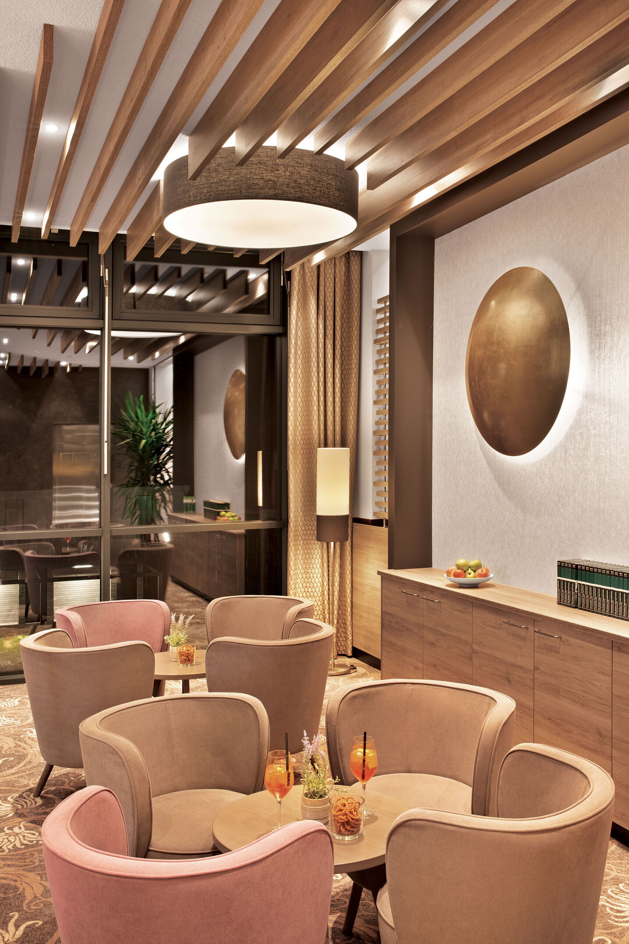 Un espace repas moderne avec des poutres en bois au plafond, un luminaire rond fixé au mur et un coin bar agrémenté d’une plante et d’un saladier de fruits.