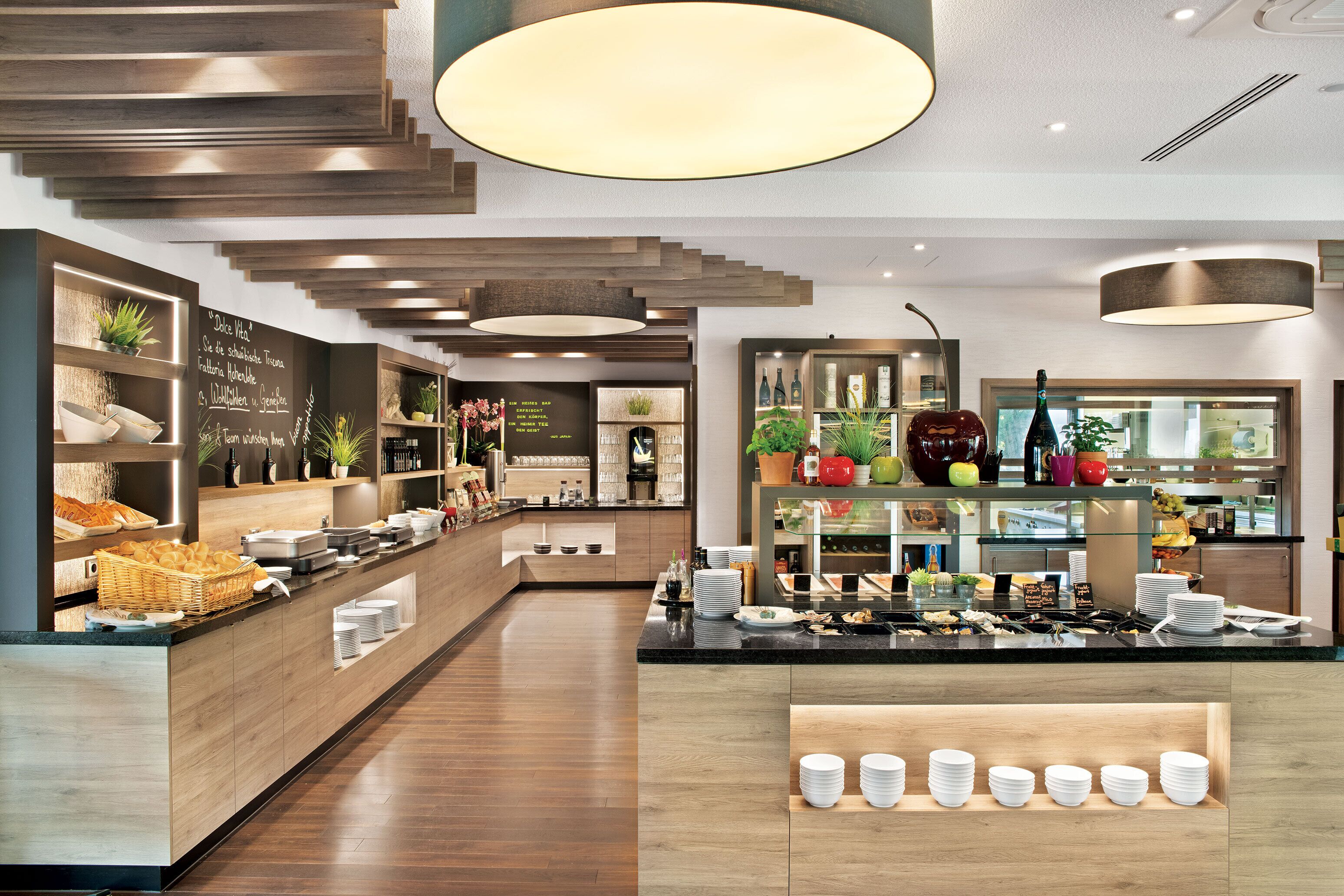 A modern hotel lobby with a central reception desk, wooden flooring, and a variety of plants and decorative items.