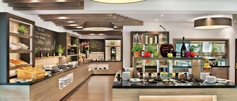 A modern hotel lobby with a central reception desk, wooden flooring, and a variety of plants and decorative items.