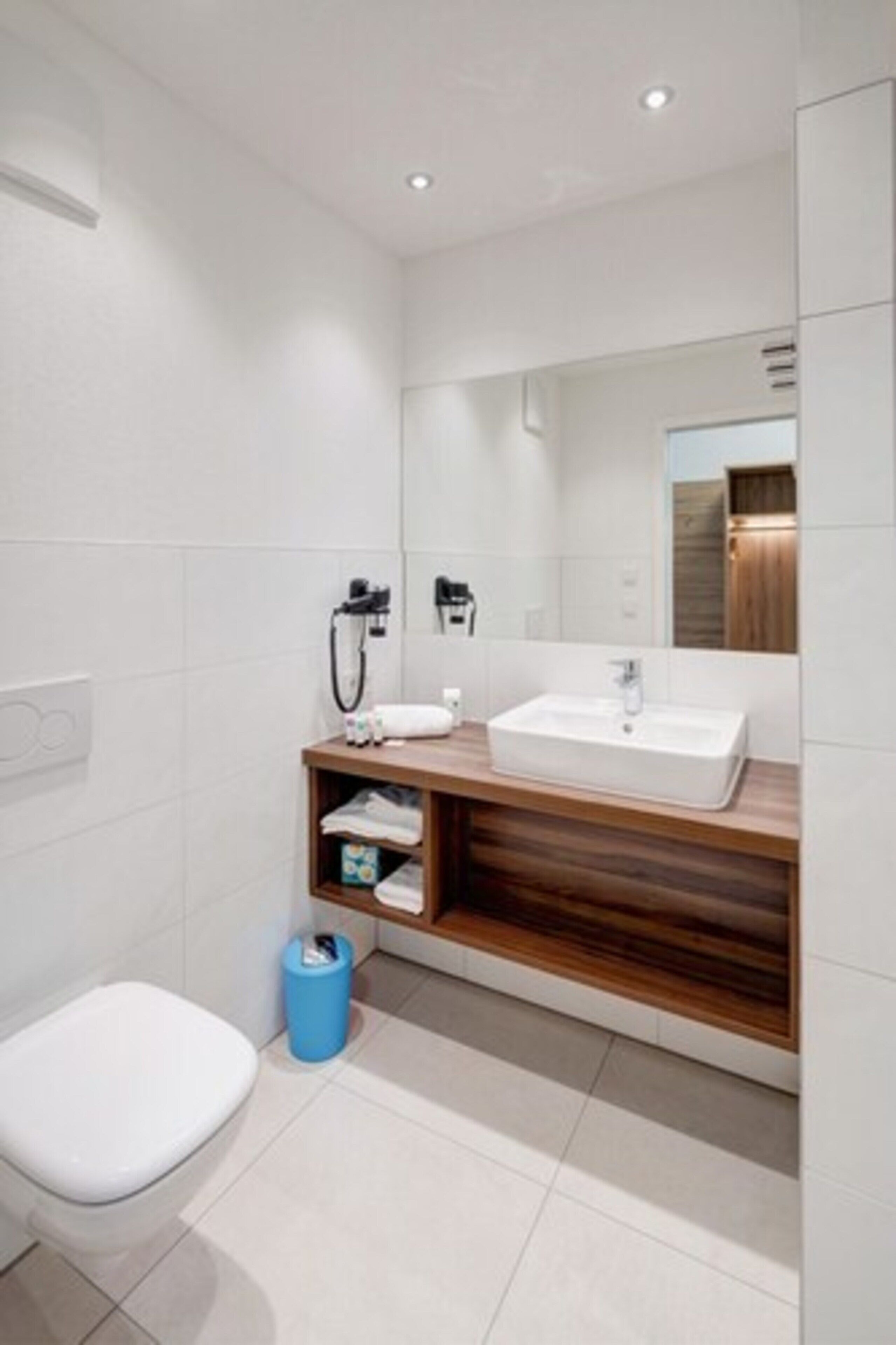 Ein modernes Badezimmer mit einer weißen Toilette, einem Holzlagerfläschchen mit Waschbecken und einem Spiegel darüber.