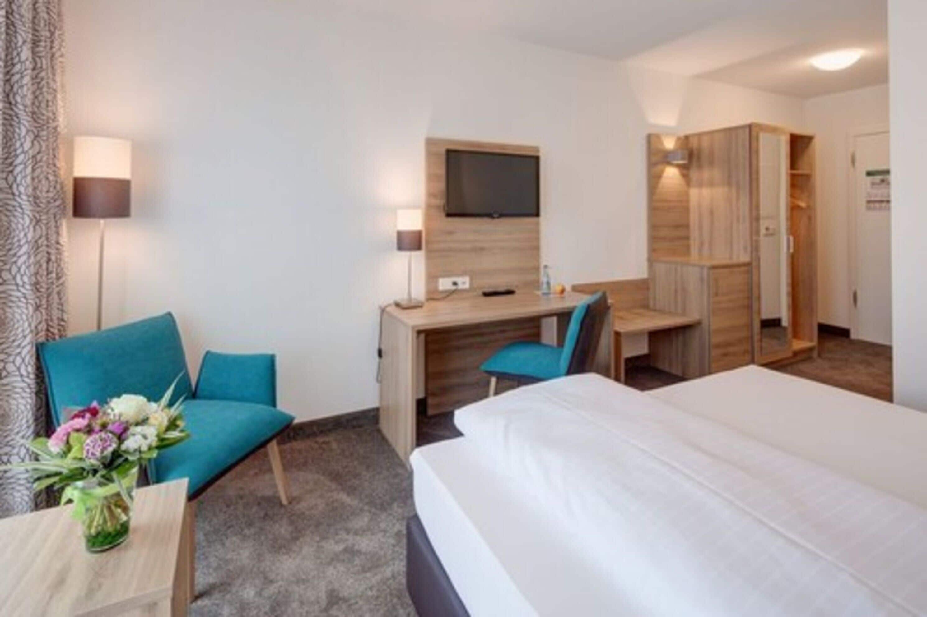 Habitación de hotel con una cama, un escritorio con silla, un televisor montado en la pared y un armario.