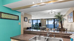 A kitchen with a granite countertop, stainless steel sink, and a dishwasher. There is a sign on the wall that reads "SEASIDE RETREAT".